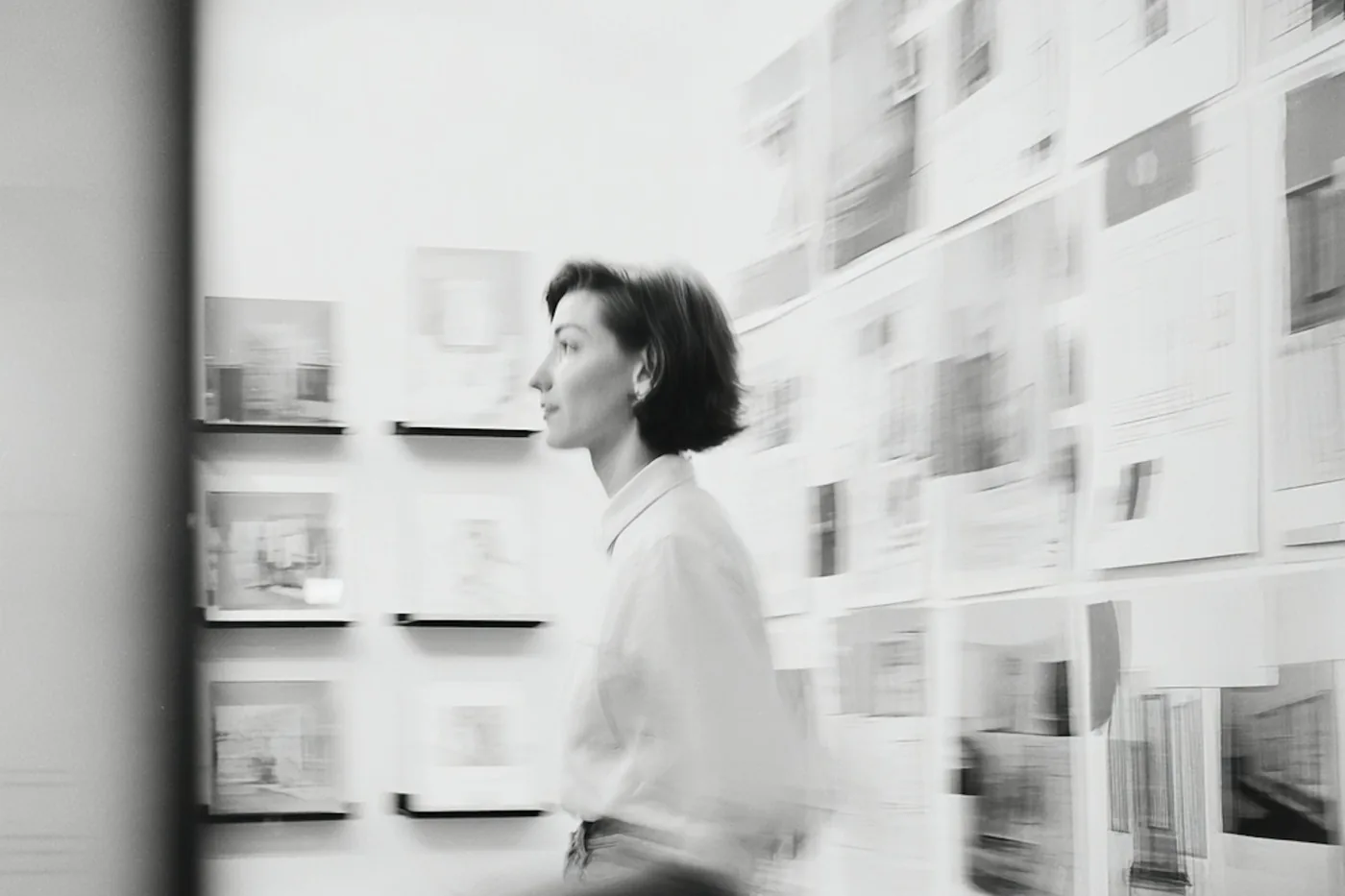 An architect walking the length of a studio wall pinned with drawings and reference sheets, caught in motion blur.